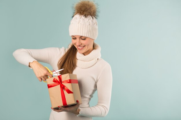 Schöne junge Frau im Winterhut mit einem Geschenk in der Hand auf einem blauen Hintergrund