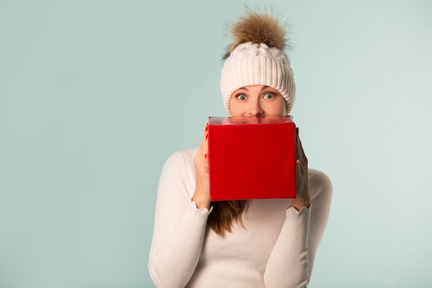 Schöne junge Frau im Winterhut mit einem Geschenk in der Hand auf einem blauen Hintergrund