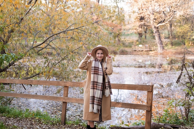 Schöne junge Frau in beige Mantelmütze und Schal am See im Herbstpark im Herbst