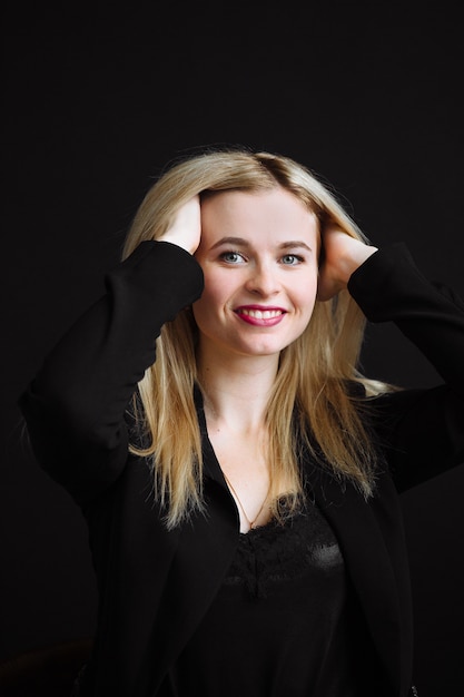 Schöne junge Frau in der schwarzen Jacke auf schwarzem Hintergrund. Hübsches blondes Mädchen