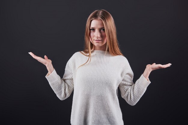 Schöne junge frau in der weißen strickjacke und in den jeans lokalisiert auf schwarzem hintergrund