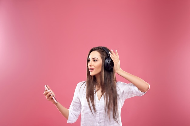 Schöne junge Frau in drahtlosen Kopfhörern, die mit dem Handy Musik hört