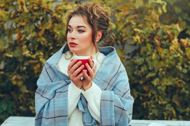 Schöne junge Frau, in eine Decke gehüllt, im Freien bei einer Tasse Tee oder Kaffee