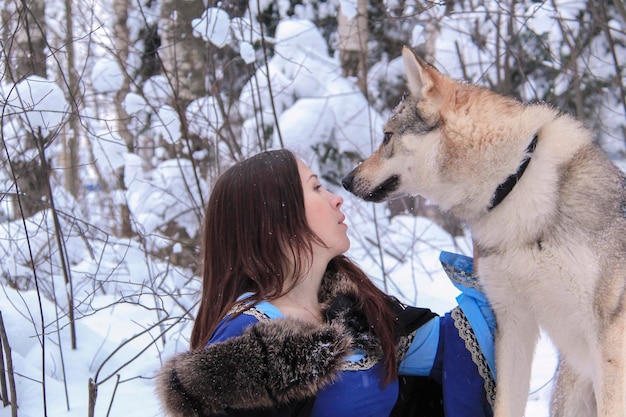 Schöne junge Frau in einem blauen Kleid kommuniziert mit einem Wolf in einem verschneiten Wald