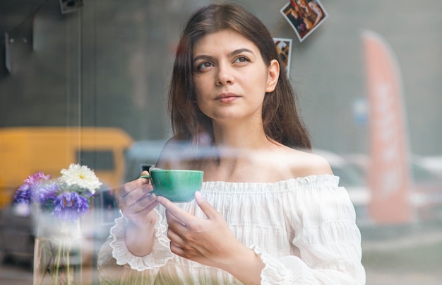 Schöne junge Frau in einem Café mit Blick auf eine Tasse Kaffee von der Straße