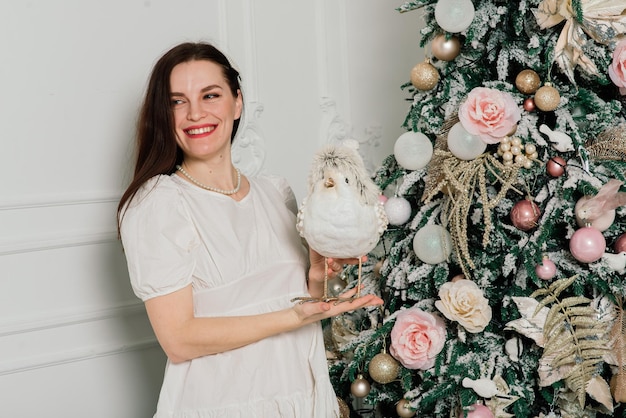 Schöne junge Frau in einem eleganten Kleid, das nahe bei Weihnachtsbaum und Geschenken steht.