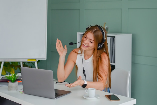 schöne junge frau in einem headset kommuniziert online mit einem laptop im bürolebensstil f