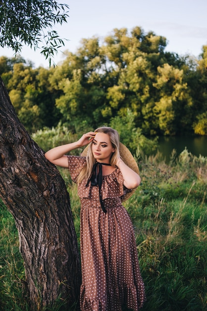 Schöne junge Frau in einem Hut und Kleid geht in der Natur im Herbst.