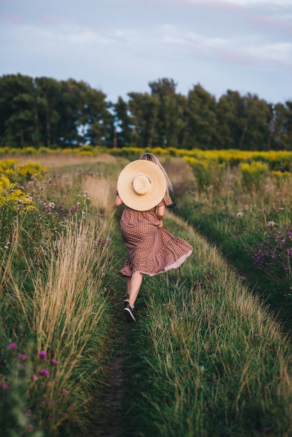 Schöne junge Frau in einem Hut und Kleid geht in der Natur im Herbst.