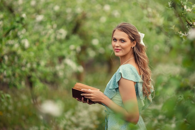 Schöne junge Frau in einem romantischen Kleid liest im Frühling in einem blühenden Garten ein zweites Buch
