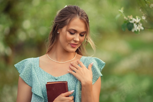 Schöne junge Frau in einem romantischen Kleid liest im Frühling in einem blühenden Garten ein zweites Buch