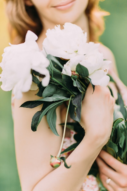 Schöne junge Frau in einem Sommerkleid mit Pfingstrosen