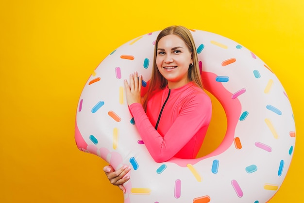 Schöne junge Frau in einem stylischen rosafarbenen Badeanzug mit einem aufblasbaren Donut-Ring auf gelbem Hintergrund