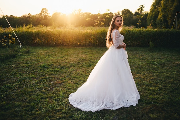 Schöne junge Frau in einem weißen Hochzeitskleid und in schwarzen Stiefeln bei Sonnenuntergang.