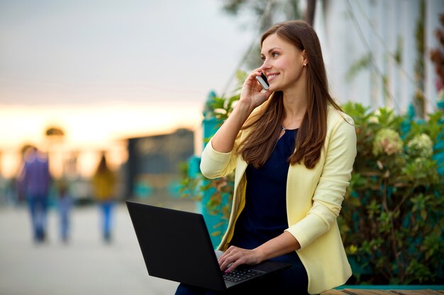 schöne junge Frau in einer gelben Jacke mit einem Laptop in einem Sommerpark