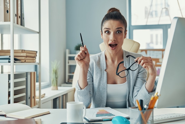 Schöne junge Frau in eleganter Freizeitkleidung, die bei der Arbeit im Büro ein Gesicht macht