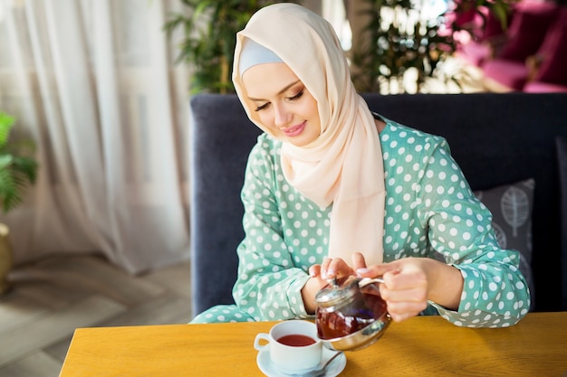 schöne junge Frau in muslimischer Kleidung trinkt Tee in einem Restaurant