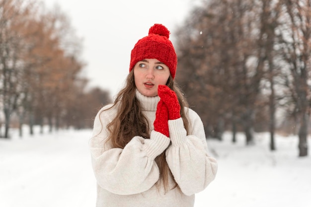 Schöne junge Frau in roter Strickmütze und Fäustlinge und Wollpullover auf der Gasse im Winterpark Porträt eines hübschen Mädchens