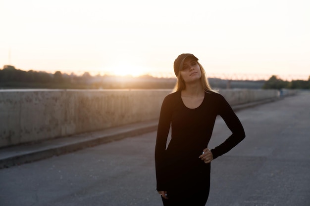 Schöne junge Frau in schwarzer Sportkleidung und Mütze bei Sonnenuntergang am Abend