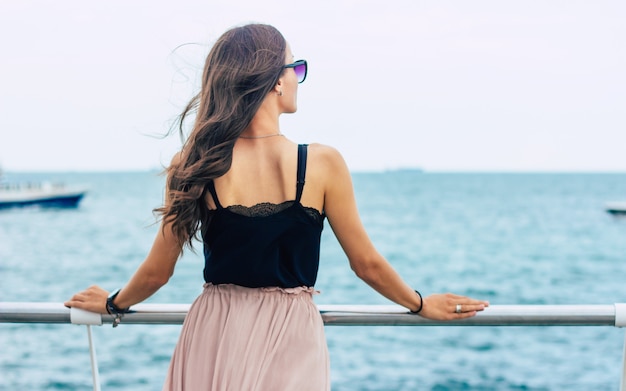 Schöne junge Frau in Sonnenbrille und Kleid auf Luxuskreuzfahrtschiff. Kreuzfahrtschiff-Urlaubsfrau, die Reisen auf See genießt. Kostenlose glückliche Frau mit Blick auf das Meer