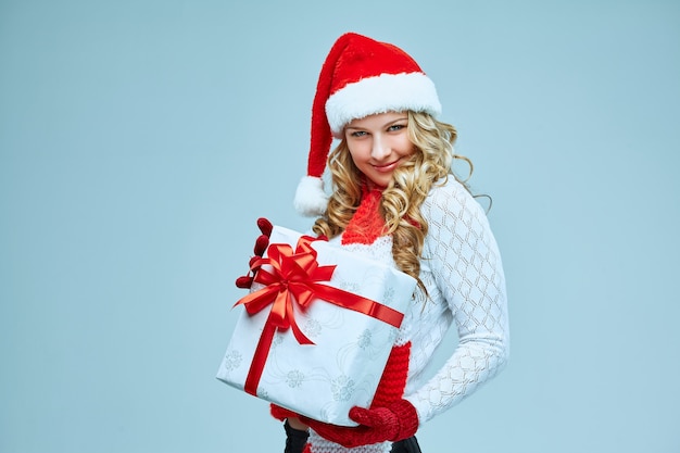 Schöne junge frau in weihnachtsmann-kleidung mit einem geschenk auf grauem hintergrund
