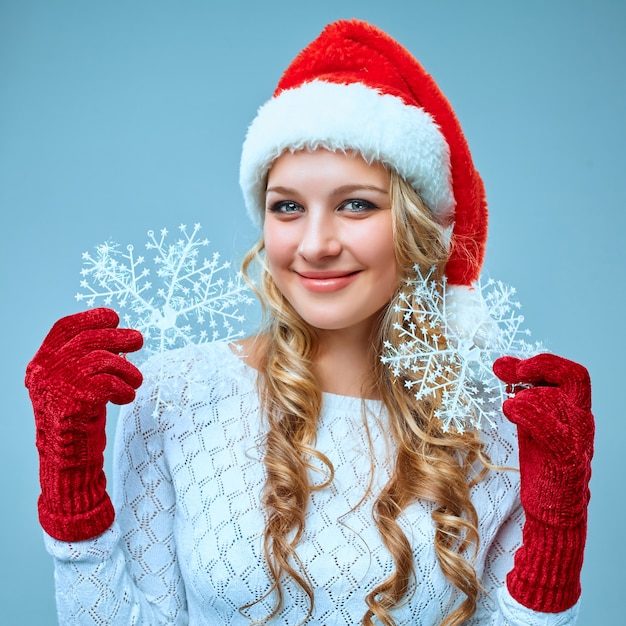 Schöne junge Frau in Weihnachtsmann-Kleidung mit Schneeflocken auf blauem Hintergrund