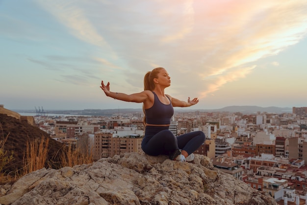 Schöne junge Frau macht Yoga im Freien, auf einem Bergrücken in der Stadt.