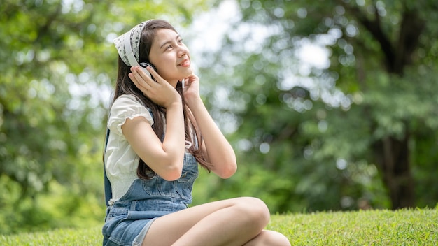 Schöne junge Frau Mädchen in beigem Hemd posiert im grünen Stadtpark Hintergrund Lächelndes Mädchen, das Musik mit Kopfhörern hört, fühlt sich berührend glücklich Menschen Lifestyle-Konzept Mock up Copy Space