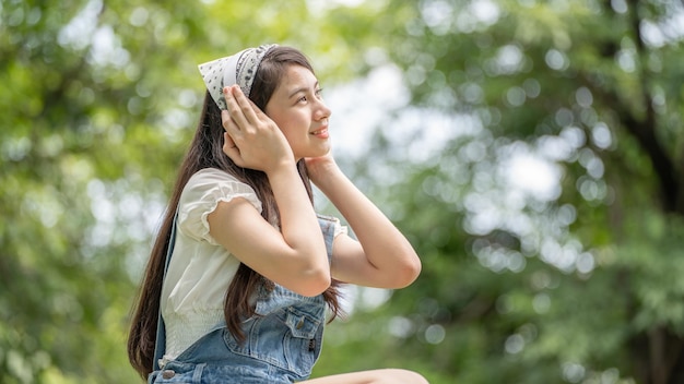 Schöne junge Frau Mädchen in beigem Hemd posiert im grünen Stadtpark Hintergrund Lächelndes Mädchen, das Musik mit Kopfhörern hört, fühlt sich berührend glücklich Menschen Lifestyle-Konzept Mock up Copy Space