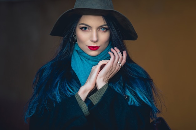 Schöne junge Frau mit blauen Haaren in schönem schwarzen Mantel, Jeans und Hut.