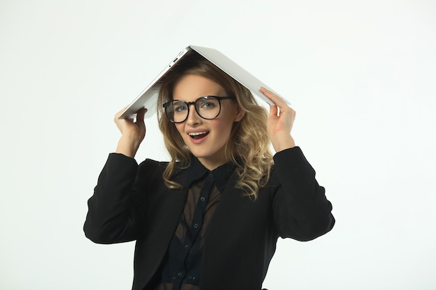 schöne junge Frau mit Brille in einem schwarzen Anzug mit einem Laptop an einer weißen Wand