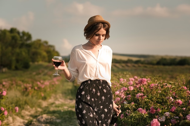 Schöne junge Frau mit dem lockigen Haar, das nahe Rosen in einem Garten aufwirft. Das Konzept der Parfümwerbung.