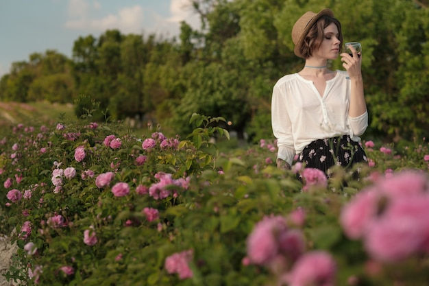 Schöne junge Frau mit dem lockigen Haar, das nahe Rosen in einem Garten aufwirft. Das Konzept der Parfümwerbung.