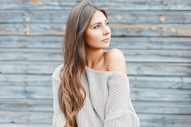 Schöne junge Frau mit der Frisur in einem Vintagen grauen Pullover nahe der blauen Wand