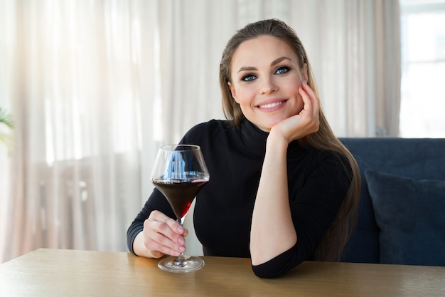 schöne junge Frau mit einem Glas Wein sitzt an einem Tisch in einem Restaurant