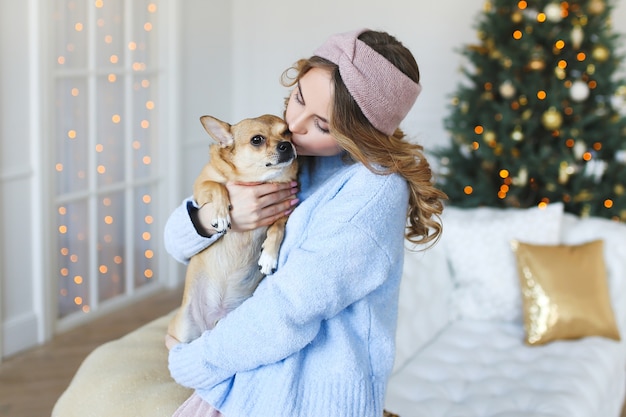Schöne junge Frau mit einem Hund auf dem Hintergrund eines Weihnachtsbaumes