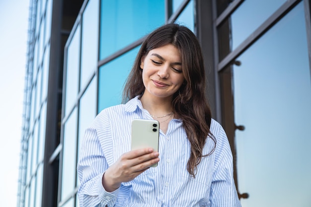 Schöne junge Frau mit einem Smartphone auf dem Hintergrund eines Glasgebäudes