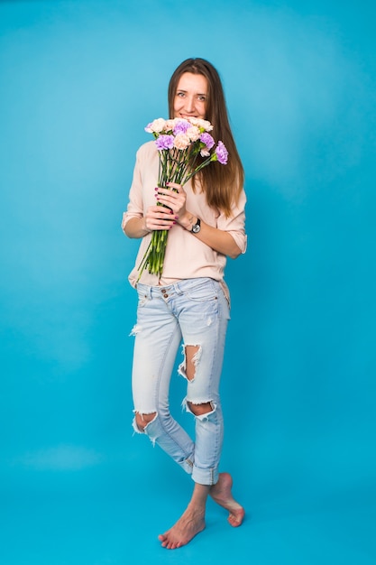 Schöne junge Frau mit einem Strauß Nelken auf blauem Hintergrund, feminin, Feier.