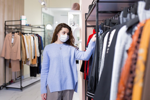 schöne junge Frau mit Freundin, die sicheres Einkaufen im Bekleidungsgeschäft während einer Pandemie in Masken tut