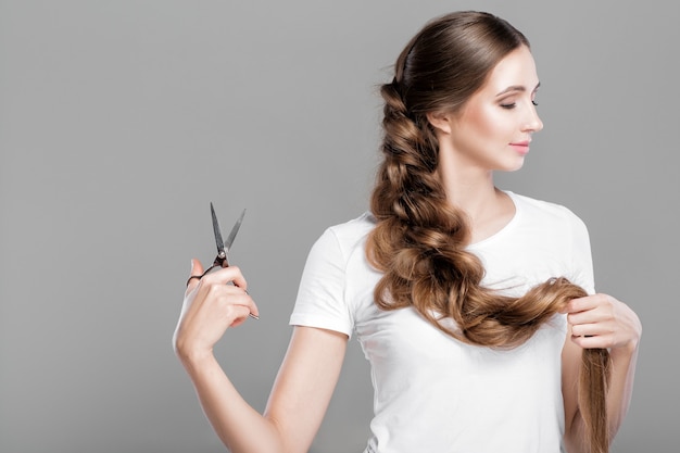 Schöne junge Frau mit geraden langen Haaren hält eine Schere für die Frisur. Platz kopieren