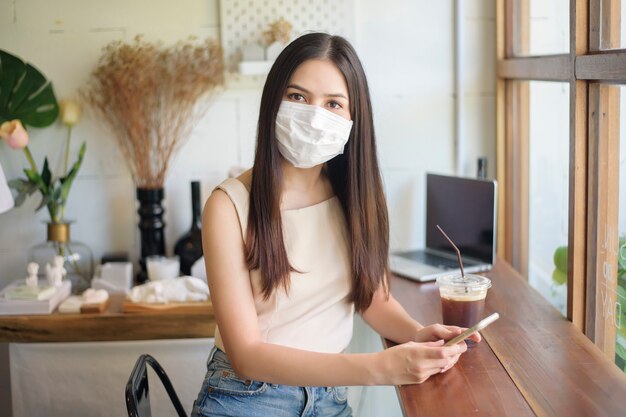 Schöne junge Frau mit Gesichtsmaske sitzt im Coffeeshop