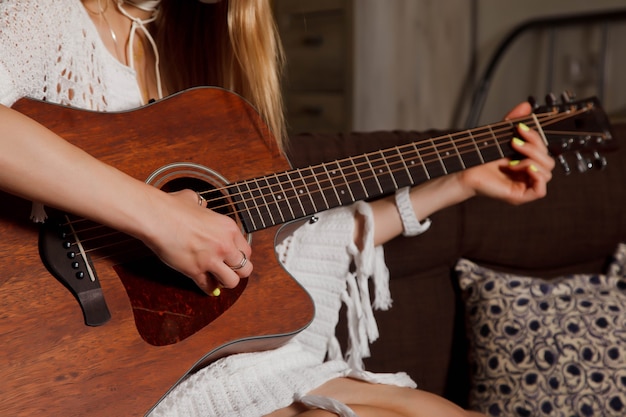 Schöne junge Frau mit Gitarre im Innenraum des Raumes. Nette Frau auf Couch mit Gitarre in ihren Händen. Konzept des Lernens zu Hause oder des Gitarrespielens zu Hause. Copyright-Bereich für Website oder Banner oder Logo