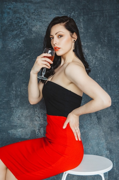 Schöne junge Frau mit Glas Wein auf grauem Hintergrund. Ein Blick in die Kamera.