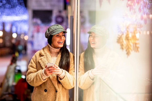 Schöne junge Frau mit Handy am Schaufenster zur Weihnachtszeit