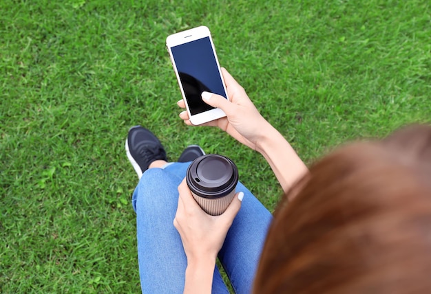 Schöne junge Frau mit Handy und Tasse Kaffee im Freien