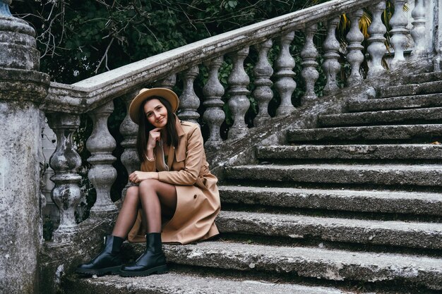 Foto schöne junge frau mit hut und jacke sitzt auf der treppe reisekonzept