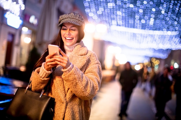 Schöne junge frau mit ihrem handy auf der straße zur weihnachtszeit