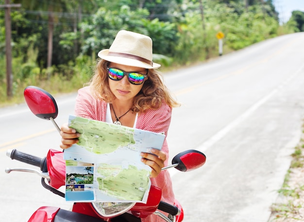 Schöne junge Frau mit Karte in der Hand und einem Motorrad auf der Straße. Reisen, Navigation, Tourismus