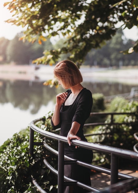 Schöne junge Frau mit Kleid, die den Sonnenaufgang am Fluss in der alten europäischen Stadt genießt Mode und Stil Sommerreisen