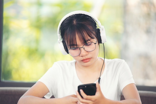 Schöne junge Frau mit Kopfhörern, die sich auf dem Zimmer entspannen, sie hört Musik mit einem Smartphone, Chill-Out und Freizeitkonzept